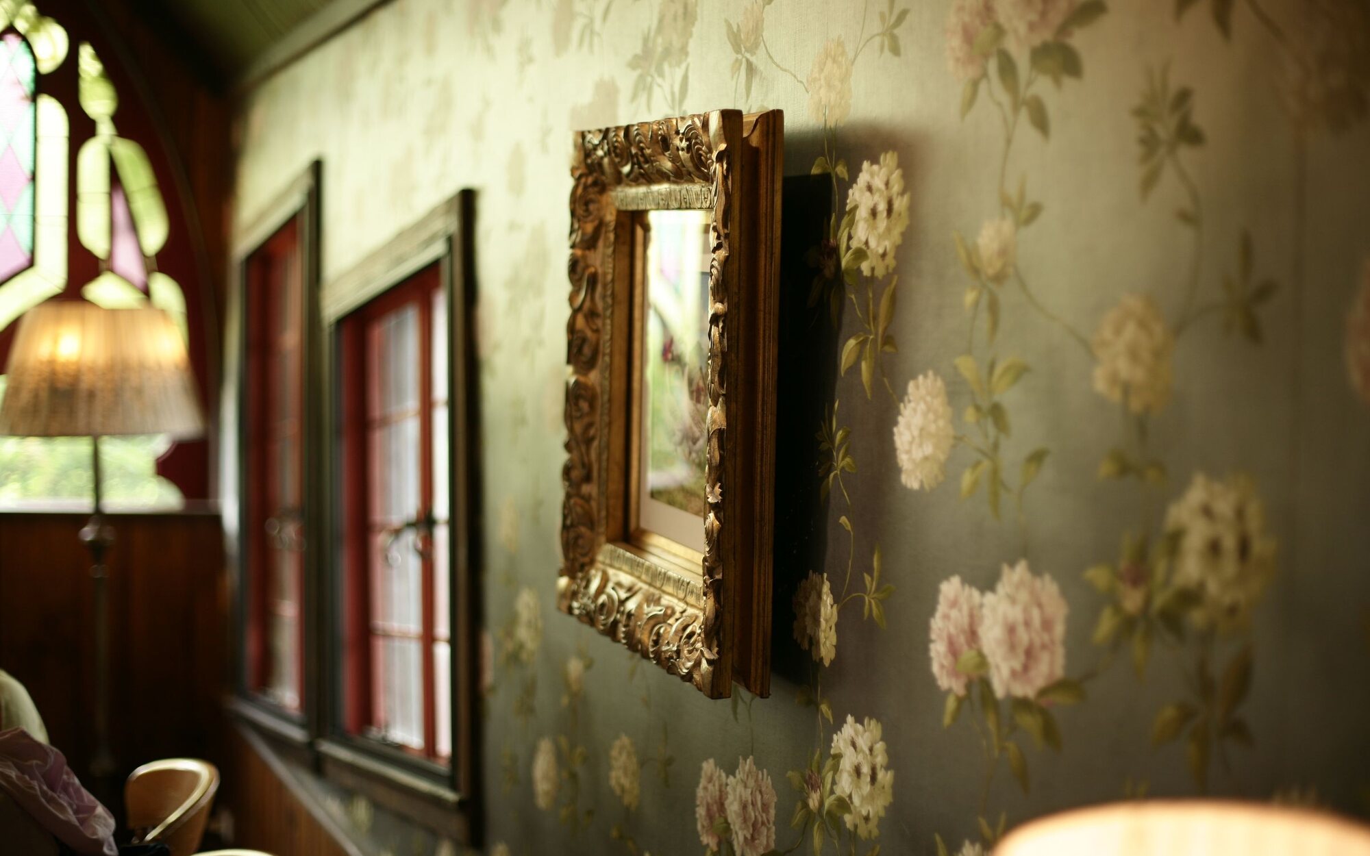 Sophisticated residential interior with sage-green floral wallpaper, a gilt-framed mirror and warm natural light