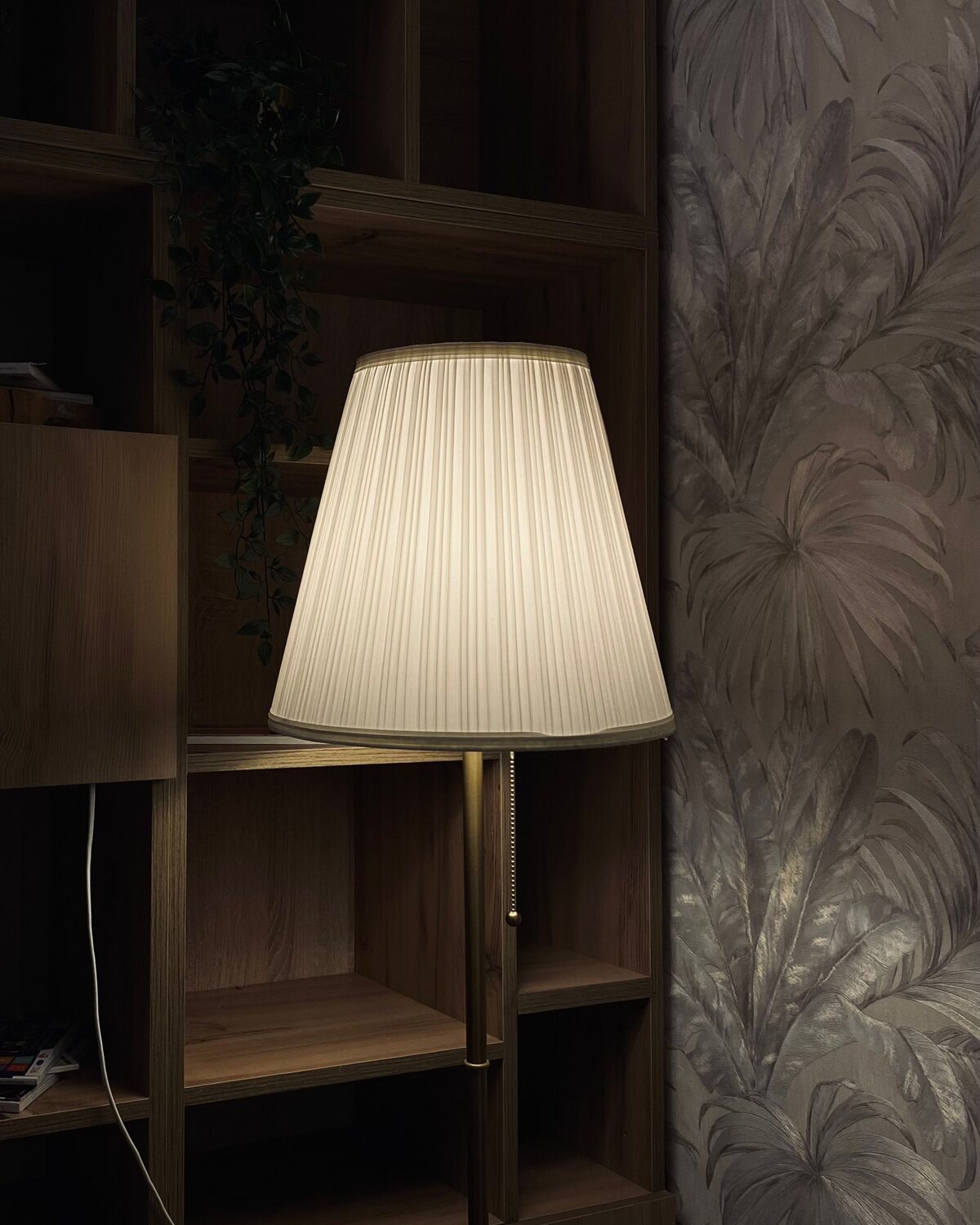 Home study nook with large-scale botanical wallpaper, shelving and a warm lamp