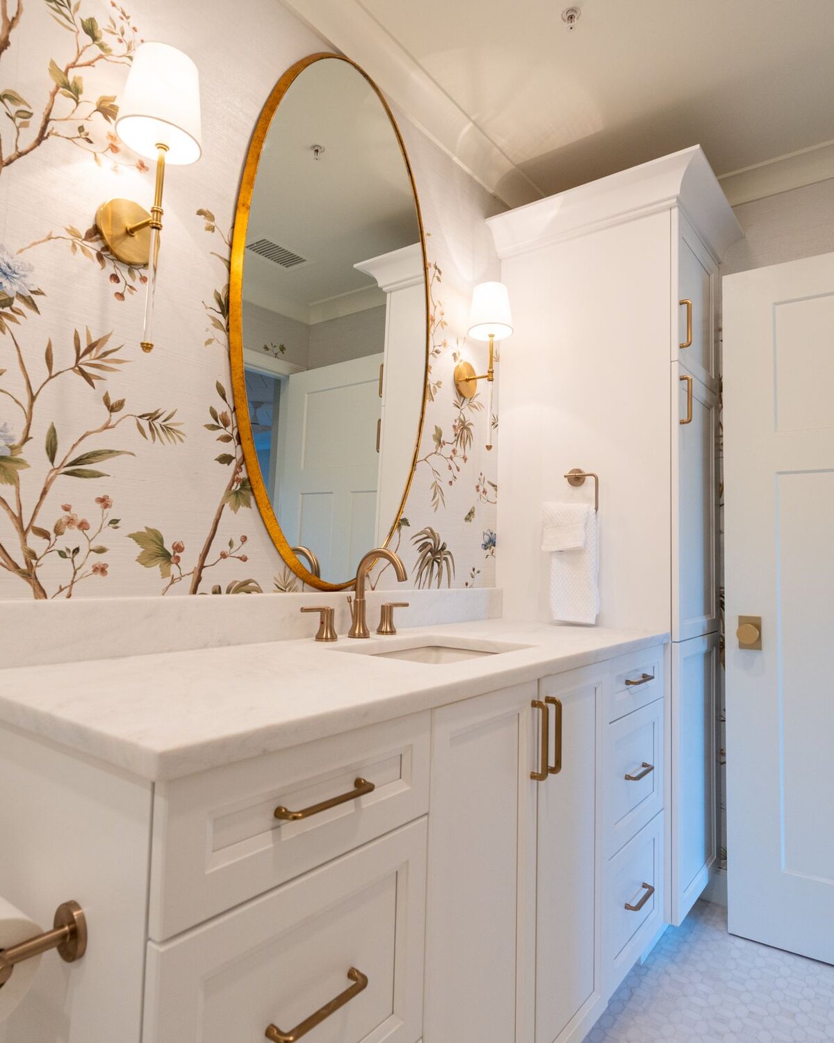 Refined powder room with chinoiserie bird wallpaper, a gilt oval mirror and brass sconces
